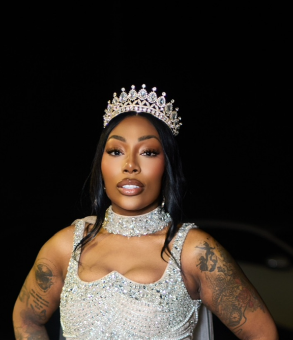 MS ELDE LORDE white dress with a tiara standing on a dark street.