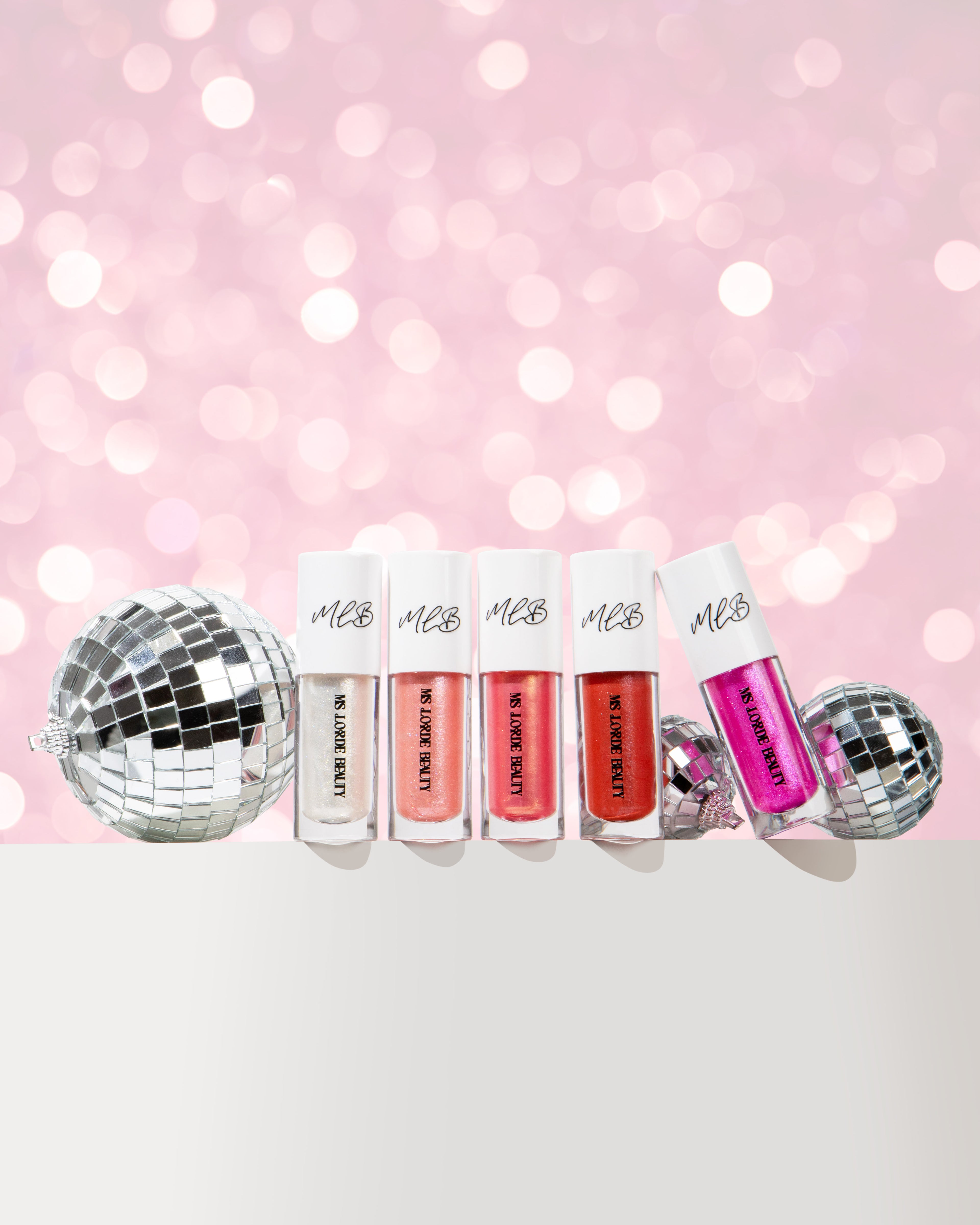 Set of lip glosses with disco balls on a pink background